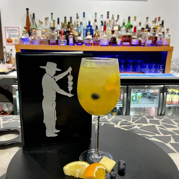 A yellow cocktail with fruit garnishes sits on a bar next to a menu and liquor bottles.