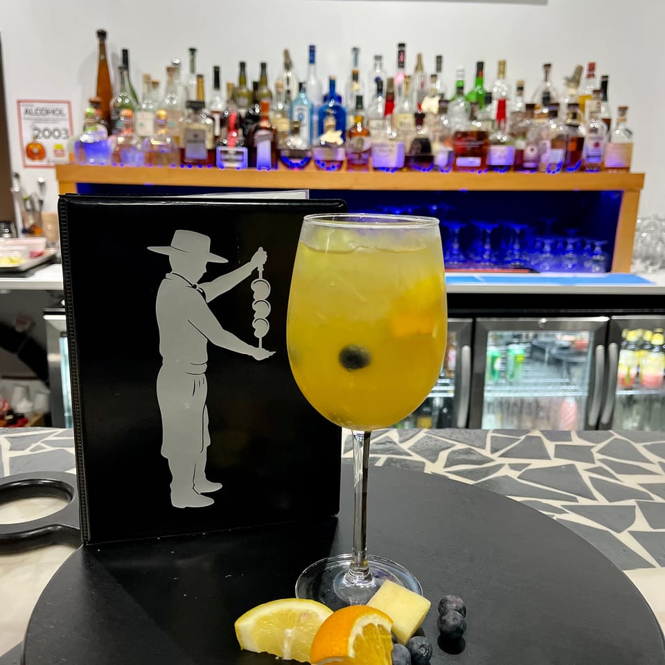 A yellow cocktail with fruit garnishes sits on a bar next to a menu and liquor bottles.