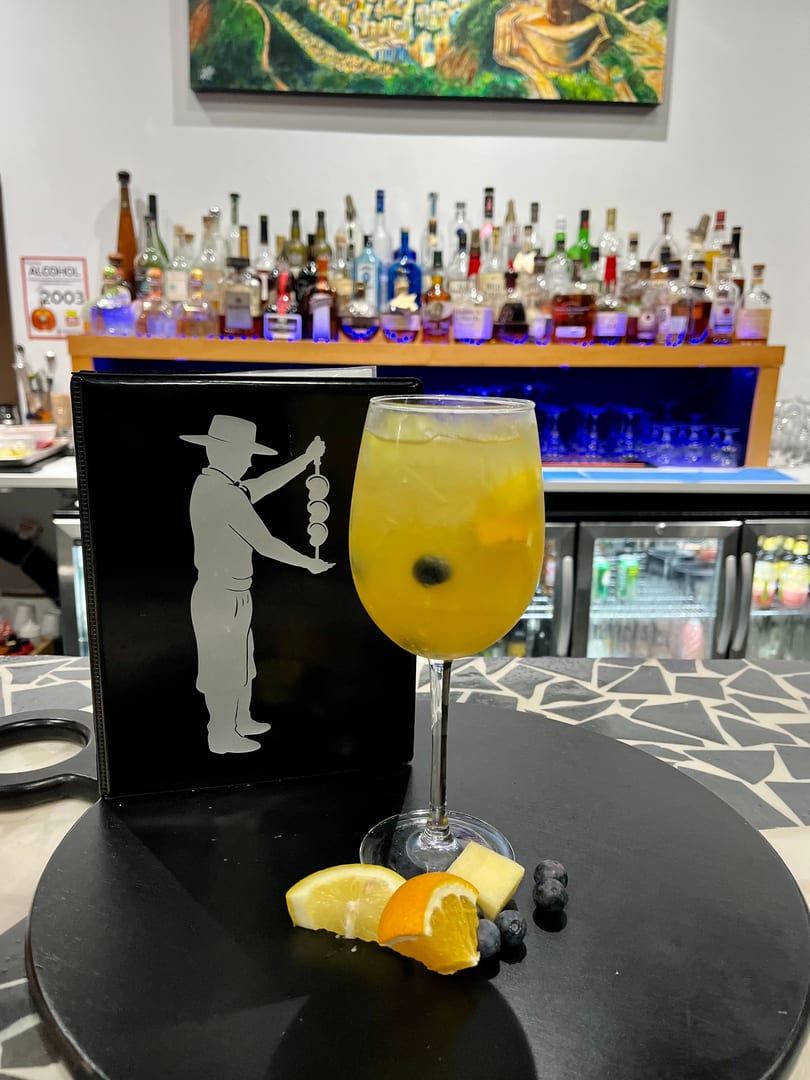 A yellow cocktail with fruit garnishes sits on a bar next to a menu and liquor bottles.