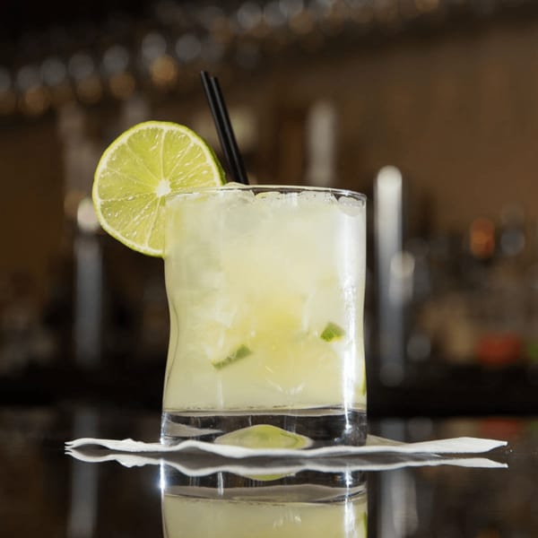 A refreshing caipirinha cocktail with a lime slice and black straw on a bar.