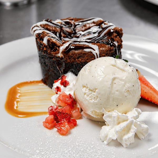 Chocolate lava cake with vanilla ice cream, whipped cream, strawberries, and caramel drizzle.